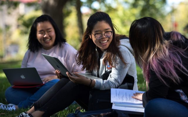 Three students laughing and working in a park.